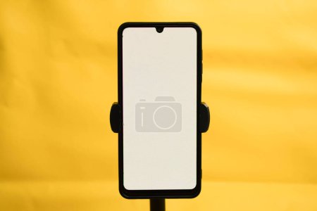 Photo for Portrait phone with white screen fixed to tripod on yellow background, for mockup design. - Royalty Free Image