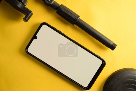 Foto de Vista superior del teléfono inteligente con pantalla blanca y partes del soporte del teléfono o mini trípode aislado sobre fondo amarillo - Imagen libre de derechos