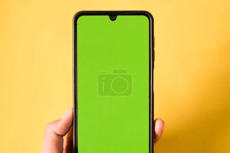 Téléchargez les photos : Main tenant téléphone portable moderne écran vert isolé sur fond jaune - en image libre de droit