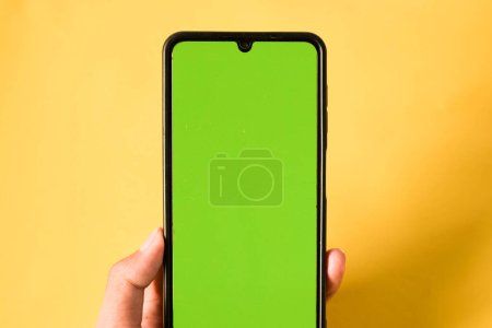 Téléchargez les photos : Main tenant téléphone portable moderne écran vert isolé sur fond jaune - en image libre de droit