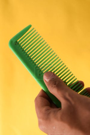 Photo for Hand hold green comb on yellow background - Royalty Free Image