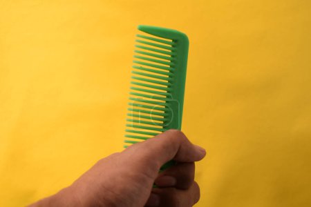 Photo for Hand hold green comb on yellow background - Royalty Free Image