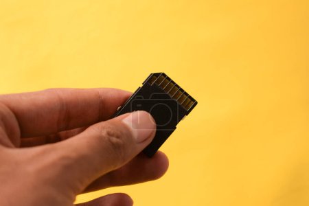 La mano sostiene la tarjeta SD para cámara réflex digital o sin espejo sobre fondo amarillo