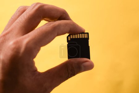 Téléchargez les photos : Main tient la carte SD pour reflex numérique ou appareil photo sans miroir sur fond jaune - en image libre de droit