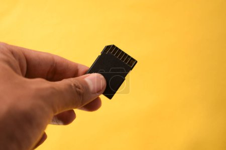 Foto de La mano sostiene la tarjeta SD para cámara réflex digital o sin espejo sobre fondo amarillo - Imagen libre de derechos