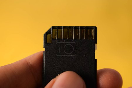 Photo for Close up hand holds SD Card for DSLR or Mirrorless camera on yellow background - Royalty Free Image