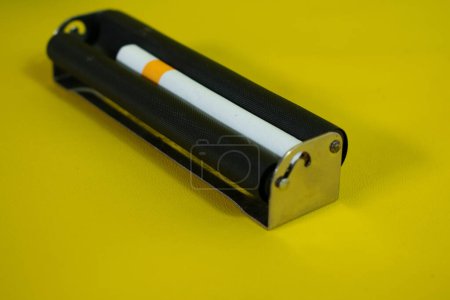 Foto de Un rodillo de metal negro para hacer cigarrillos, rodillo de cigarrillo hecho a mano sobre fondo amarillo - Imagen libre de derechos