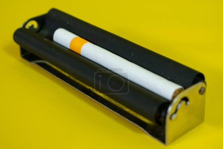 Foto de Un rodillo de metal negro para hacer cigarrillos, rodillo de cigarrillo hecho a mano sobre fondo amarillo - Imagen libre de derechos