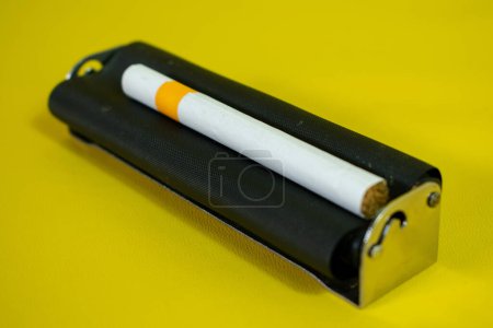 Photo for A black metal roller for make cigarette, cigarette roller handmade on yellow background - Royalty Free Image