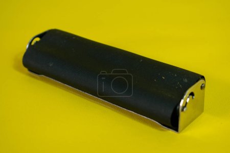 Téléchargez les photos : Un rouleau en métal noir pour faire la cigarette, rouleau de cigarette fait à la main sur fond jaune - en image libre de droit