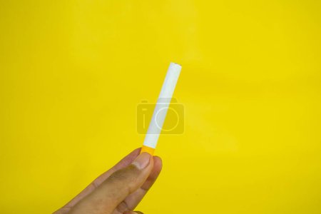 Téléchargez les photos : Une main d'homme tient une cigarette faite à la main sur fond jaune - en image libre de droit