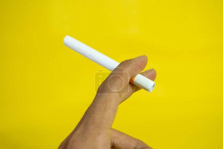 Foto de Una mano de hombre sostiene un cigarrillo hecho a mano sobre fondo amarillo - Imagen libre de derechos