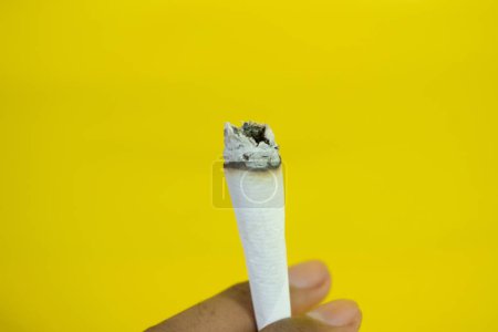 Foto de Una mano de hombre sostiene un cigarrillo hecho a mano sobre fondo amarillo - Imagen libre de derechos