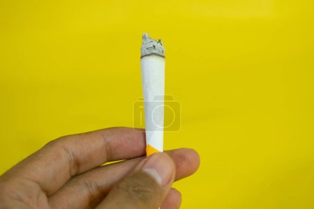 Téléchargez les photos : Une main d'homme tient une cigarette faite à la main sur fond jaune - en image libre de droit