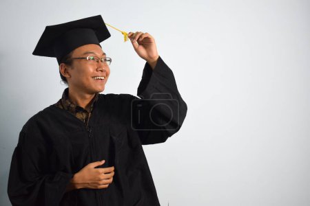 Téléchargez les photos : Expressive de l'indonésie adulte homme porter robe de graduation, chapeau et lunettes isolées sur fond blanc, expressions de la graduation portrait - en image libre de droit