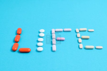 Foto de Palabra de vida de las píldoras coloridas de la medicina aisladas en fondo azul, suplemento, vitamina, colorido - Imagen libre de derechos