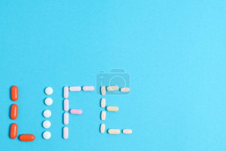 Téléchargez les photos : Mot de vie de pilules de médecine colorée isolé sur fond bleu, supplément, vitamine, coloré - en image libre de droit