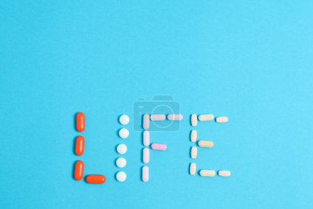 Téléchargez les photos : Mot de vie de pilules de médecine colorée isolé sur fond bleu, supplément, vitamine, coloré - en image libre de droit