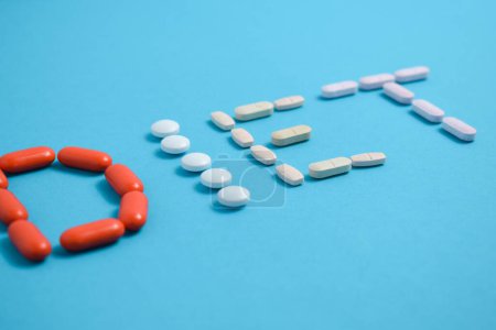 Téléchargez les photos : Mot de régime de pilules de médecine colorée isolé sur fond bleu, supplément, vitamine, coloré - en image libre de droit