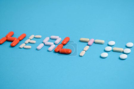 Téléchargez les photos : Mot de santé de pilules de médecine colorée isolé sur fond bleu, supplément, vitamine, coloré - en image libre de droit