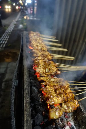 Téléchargez les photos : Nourriture typique indonésienne appelée Satay de poulet, viande de poulet croisée au bâton de bambou grillé avec du charbon de bois brûlé et servi avec de la sauce aux arachides sucrée. - en image libre de droit