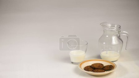 Téléchargez les photos : Concept de fond pour la journée mondiale du lait, image une cruche de verre de lait et des biscuits sur la table, isolé en arrière-plan blanc, espace de copie. - en image libre de droit