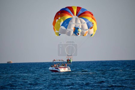 Téléchargez les photos : 2 personnes Parachutisme dans le ciel bleu, remorqué par un bateau. Parasol multicolore. Arrivée à terre par le bateau. - en image libre de droit