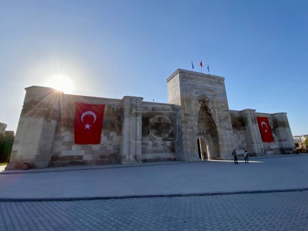 Photo for Caravanserai, Sultanhani, Turkey. Exterior, blue sky and Tuyrkish Flag, sun coming up behind. - Royalty Free Image