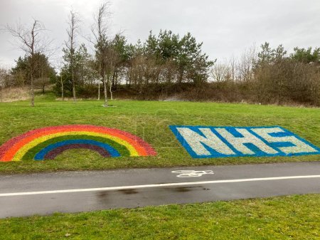 Photo for NHS Logo with Rainbow painted on grass bank.Derby, England, UK. February 20, 2021. - Royalty Free Image