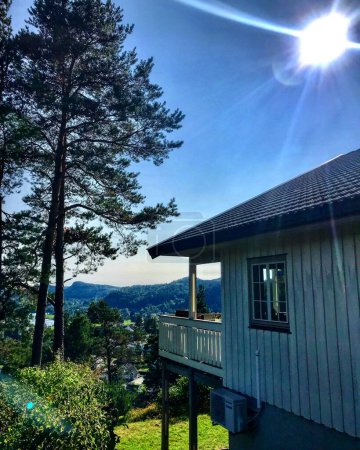 Foto de Una típica casa de madera noruega con vistas a árboles y montañas bajo un sol ardiente. Kristiansand, Noruega. - Imagen libre de derechos