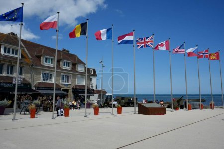 Photo for National Flags in The Town Centre Square, with a US Army WW2 Half Track. Arromanches-les-Bains, France, July 6, 2023. - Royalty Free Image