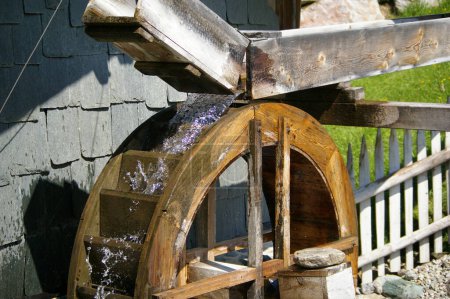Fresh cold clear water running over a wooden waterwheel in the sunlight. 