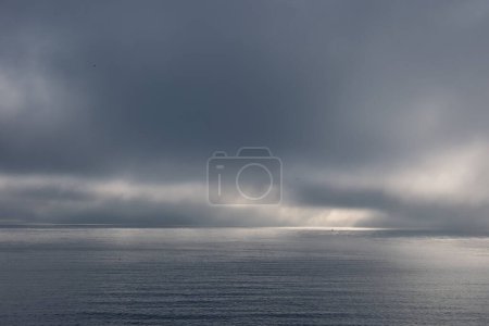 Photo for A fog bank lies offshore, the rolling clouds are low above the water. Foggy morning in calm sunny conditions The golden rays of the sun illuminate the scene. Soft light. Flat surface and glassy water - Royalty Free Image