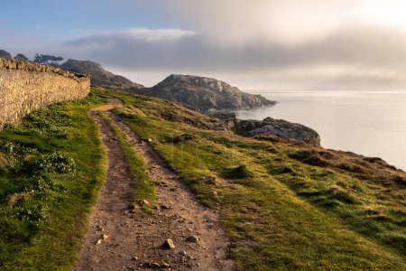 Photo for Hiking trail on Howth Island, Dublin, Ireland. Above the sea there is fog below a blue sky. The golden rays of the sun illuminate the scene. Soft light. High quality photo - Royalty Free Image