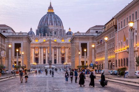 Photo for An almost empty and abandoned St. Peters Square during Covid pandemic. Illuminated St. Peters basilica and pinkish clouds at sunset.Long shutter speed blurs the single visitors. Vatican City, Rome - Royalty Free Image