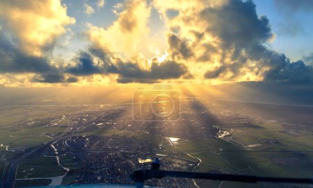 Photo for Sun rays shining through clouds above Amsterdam. Seen looking south, with the Dutch coastline and downtown city of Amsterdam. Birds eye photo. High quality photo - Royalty Free Image
