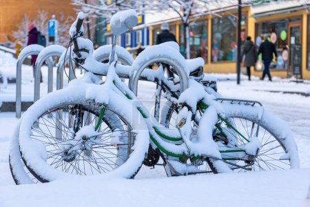 Fahrräder, die auf einem Parkplatz mit einer dicken Schicht Neuschnee abgestellt waren. Urbane Szenerie im weichen Winterlicht im Hintergrund. In Helsinki, Finnland. Hochwertiges Foto