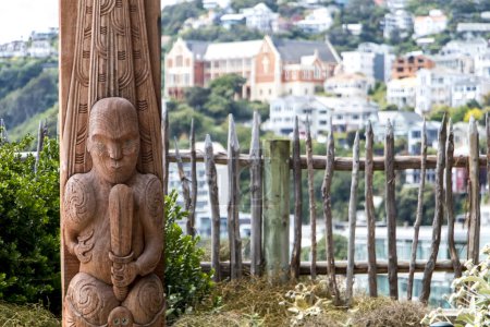 Téléchargez les photos : Statue maorie rouge en milieu urbain à Wellington, Nouvelle-Zélande. Maisons lumineuses et colorées au foyer doux en arrière-plan. Photo de haute qualité - en image libre de droit