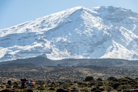 Photo for Mount Kilimanjaro with native porters carrying pack on their heads. Hiking trail to the top. Mountain top covered in Snow. High quality photo - Royalty Free Image