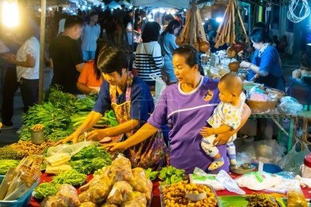 Photo for Thai night market in Chiang Rai. Sales women with child on hip and fresh wares in stall. High quality photo - Royalty Free Image