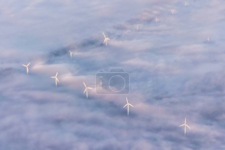 Photo for Aerial image of windmills, windturbines sticking out of the fog clouds in morning light. Vibrant colours, patterns and ripples in the clouds by the flowing fog. High quality photo - Royalty Free Image