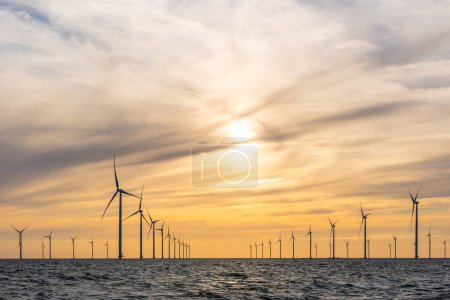 Photo for Offshore wind farm with many curving rows of high windmills, IJsselmeer, the Netherlands. Orange evening sky with moody clouds. - Royalty Free Image
