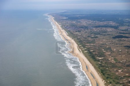 Aerial image of the Dutch coastline with breaking waves on the golden beach and sand dunes protecting The Netherlands . High quality photo