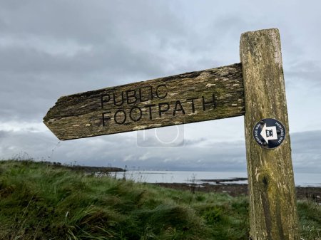 Photo for Wooden sign with carved letters saying public footpath. In front of eroded cliffs and the North Sea at a beach. In Whitley Bay, Newcastle, England, UK. High quality photo - Royalty Free Image