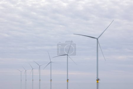 Off shore wind turbines or wind mills at a flat, calm sea, no wind. Grey cloudy sky.High quality photo