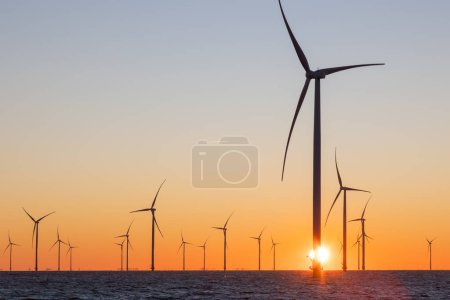 Off shore wind turbines or wind mills at sea during sunrise. Many high windturbines with a orange rising sun. High quality photo