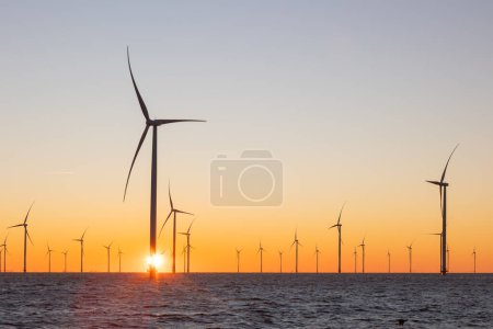 Foto de Turbinas eólicas en alta mar o molinos de viento en el mar durante el amanecer. Muchos aerogeneradores altos con un sol naranja naciente. Foto de alta calidad - Imagen libre de derechos