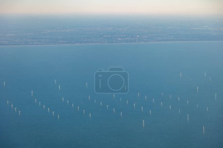 Aerial image of large off shore wind farm with turbines at sea before Dutch coast, shore of Holland in the distance . High quality photo