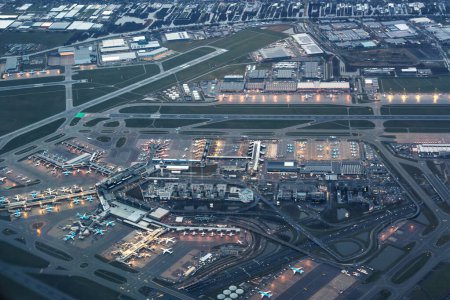 Aerial high altitude view of an Amsterdam airport at night, dusk, dawn. Many parked airplane, aeroplane and planes. Runway with hangers and many buildings illuminated. High quality photo