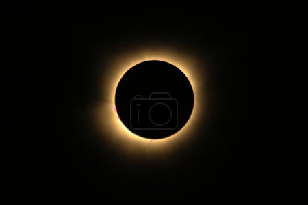 Total solar eclipse of April 8th 2024 with the sun peaking from behind the moon creating. a diamond ring effect. Red prominences and bright corona during totality. High quality photo